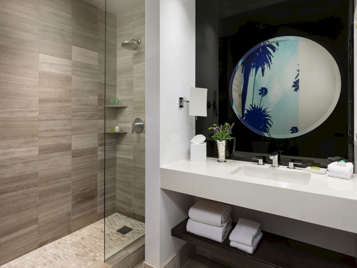 A modern bathroom features a glass shower, a sink with a mirror, and neatly folded towels.