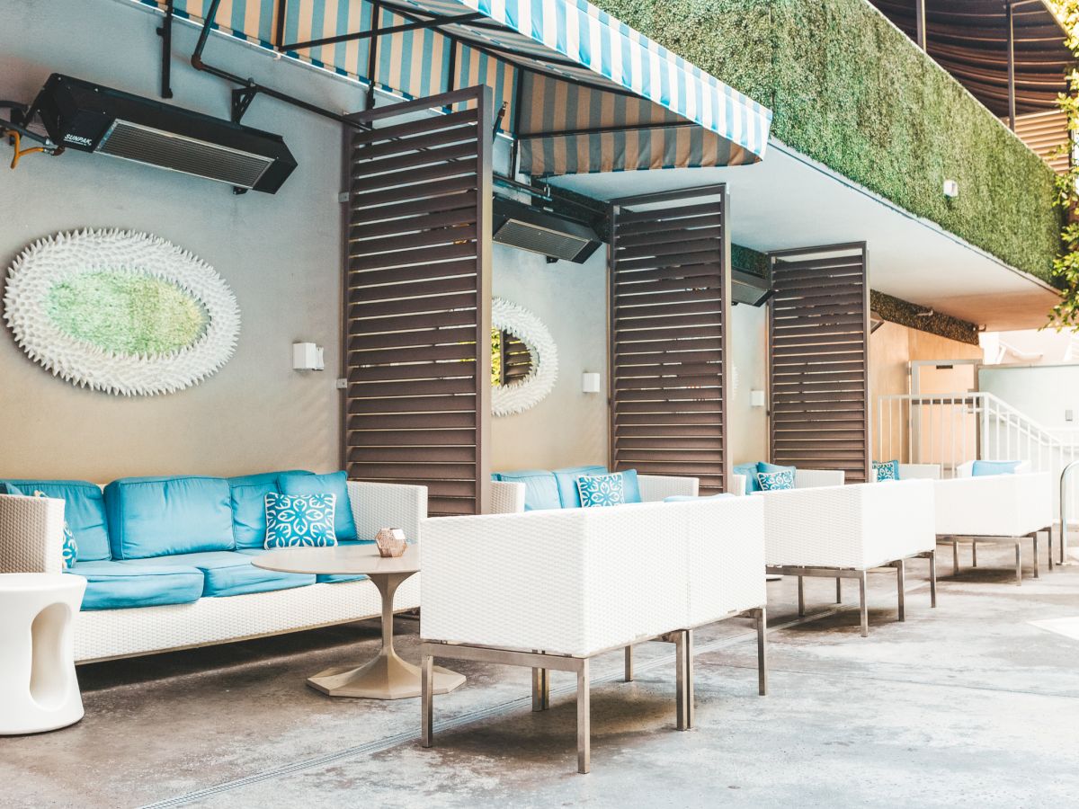 Outdoor seating area with blue cushions, decorative pillows, white wicker furniture, and a striped awning.