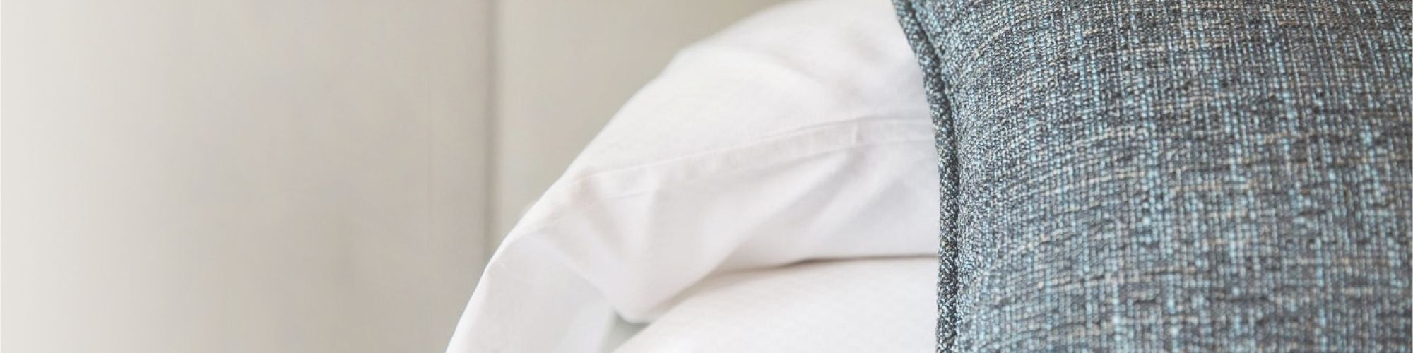 A neatly made bed with white pillows and a textured blue-grey decorative pillow on top.